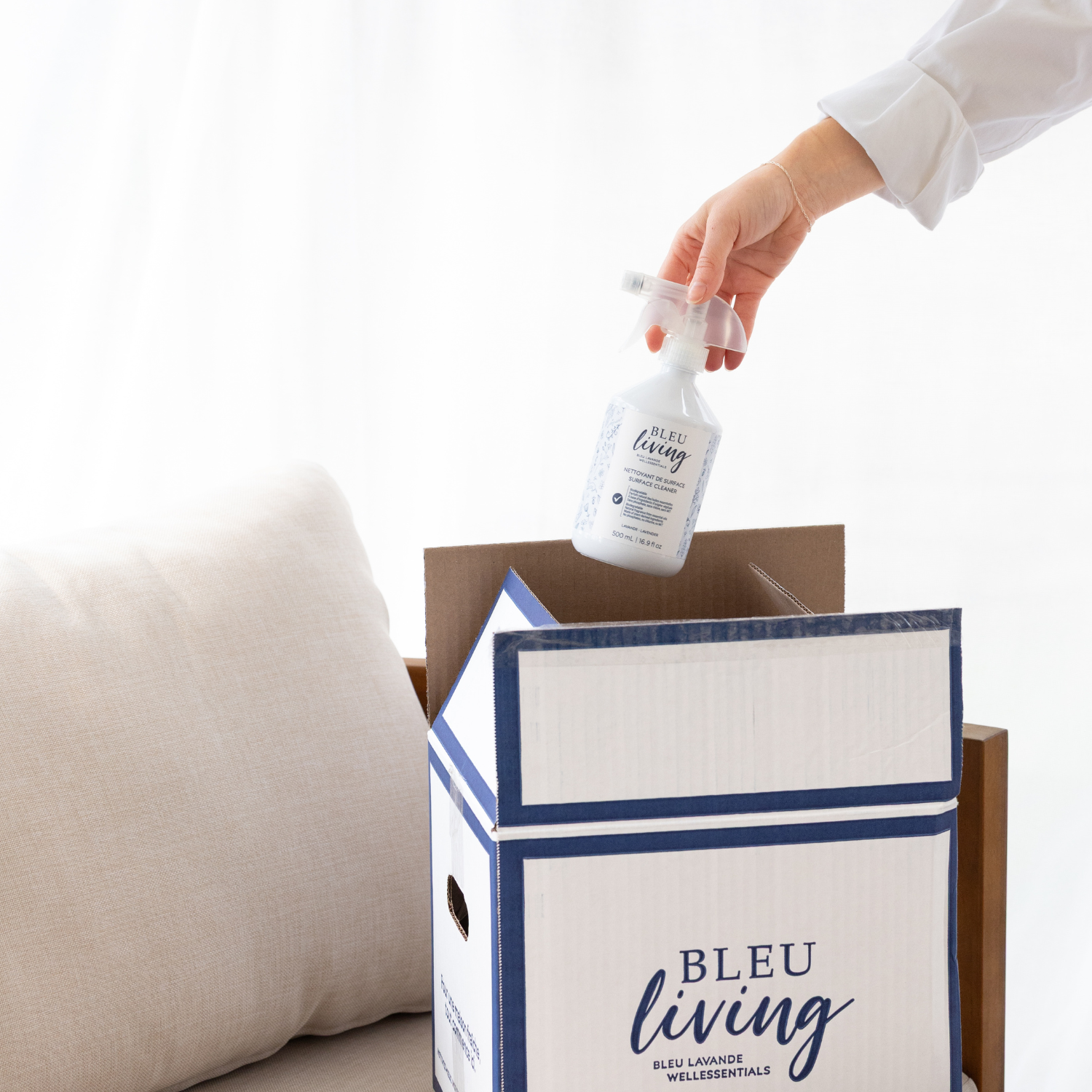 Main qui prend un nettoyant de surface de la boîte Bleu Living, un ensemble de produits ménagers québécois pour la maison