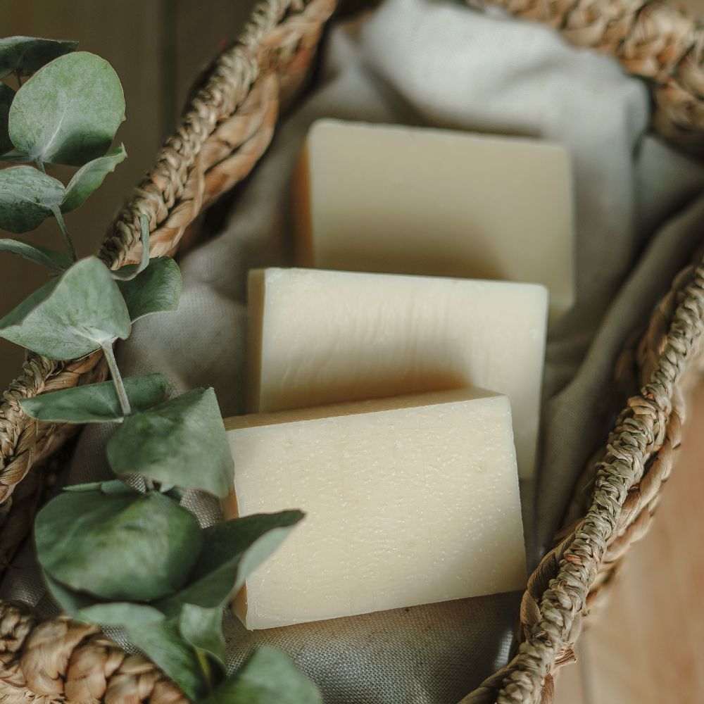 Trois savons artisanaux lavande-eucalyptus sur un tissu blanc dans un panier en osier avec une branche d'eucalyptus